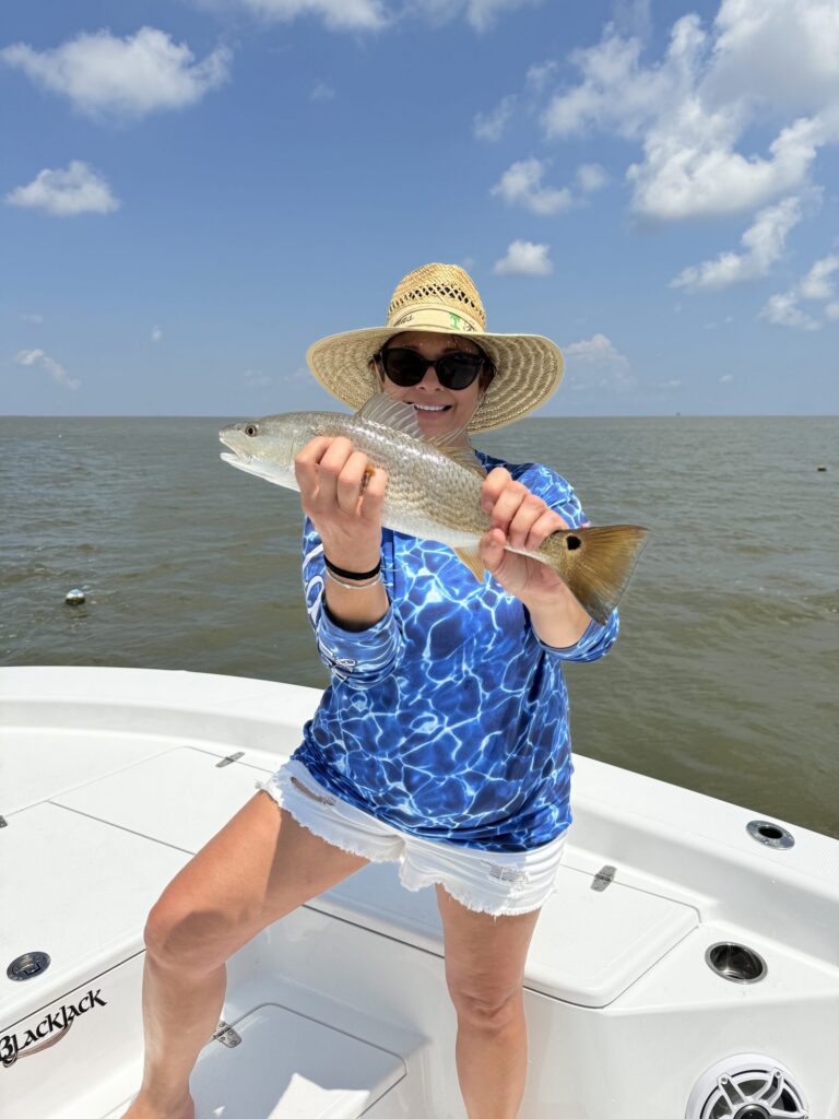 A guest in a straw hat holding a redfish on the deck of the Blackjack, the charter boat