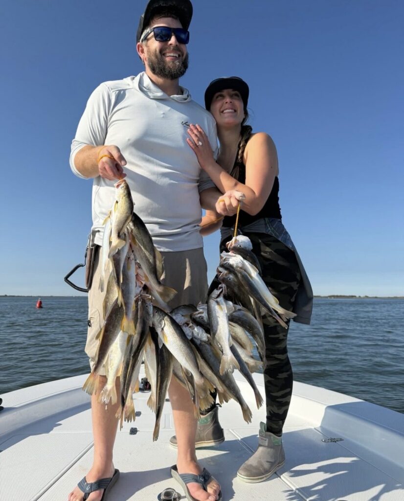 A smiling couple holding stringers of freshly caught fish on the boat